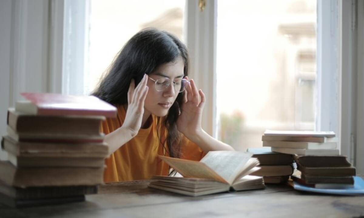 Student studying with books at a desk, preparing for exams while planning ahead for student loans and repayment after graduation.