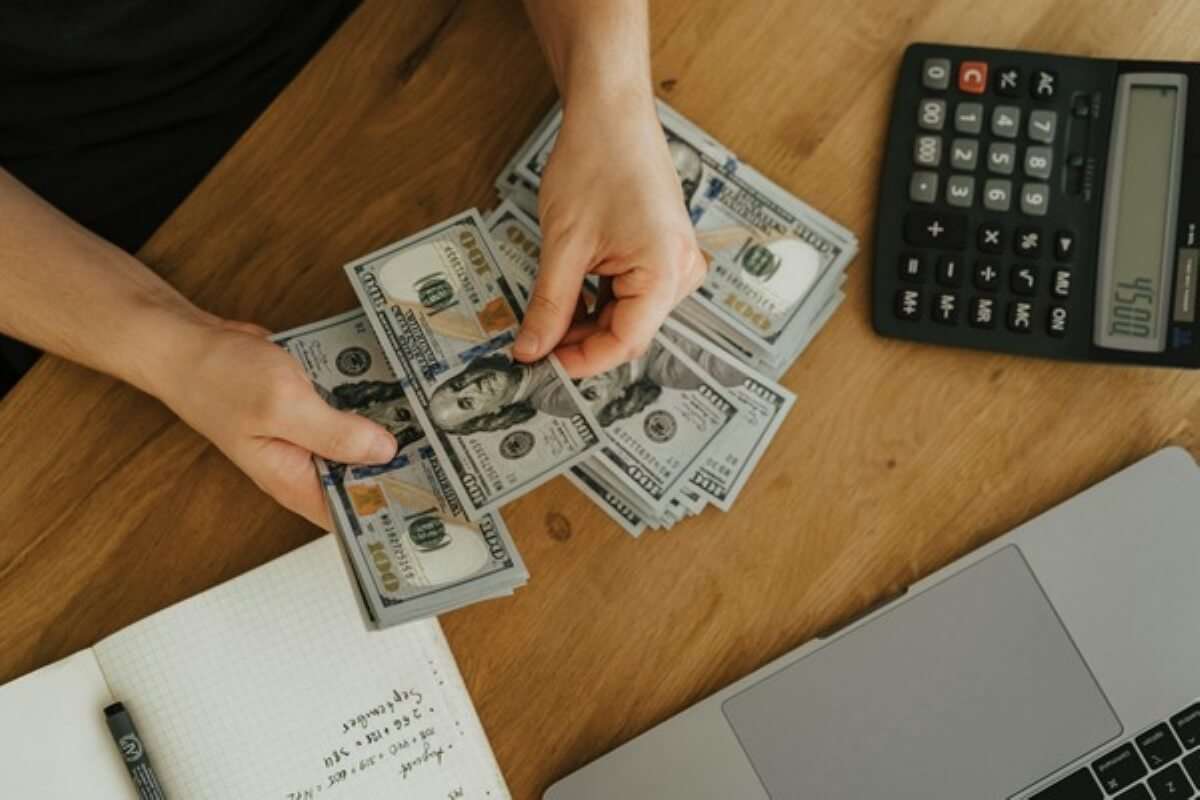 Person counting cash beside a calculator and laptop while planning a budget for student loans and repayment after graduation.