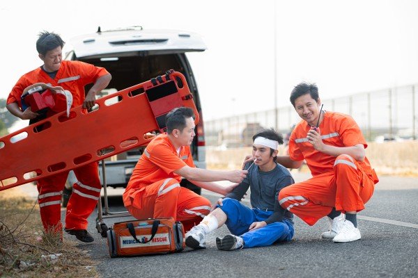 Paramedics treating an injured worker at the roadside, highlighting the migrant workers new medical insurance rules in Singapore.