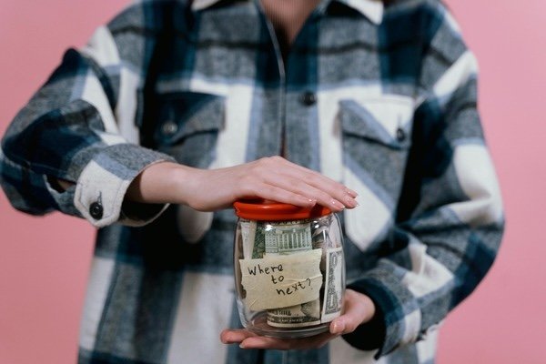 A person holding a glass jar with paer bills