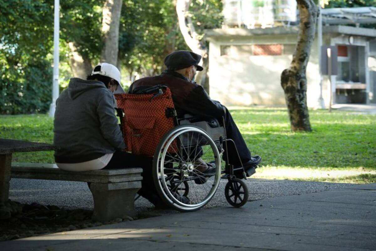 Elderly wheelchair user with a caregiver in a park, illustrating how disability income insurance can provide income support during long-term disability.