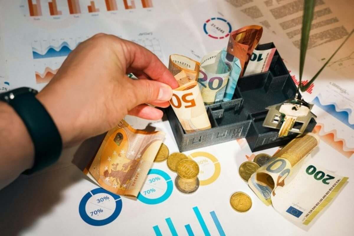 Hand placing cash into a house-shaped savings organiser, illustrating financial planning before buying insurance.