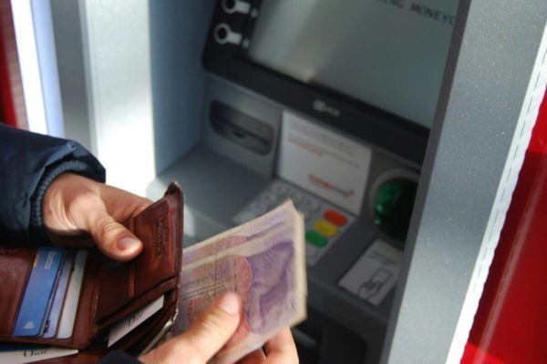 Person withdrawing cash from an ATM using funds from a joint bank account.