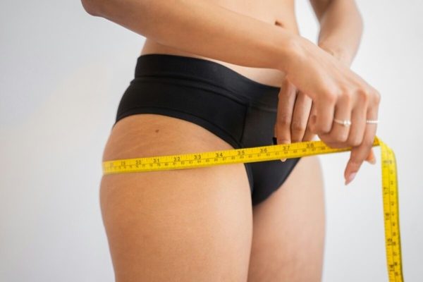 Person measuring waist with a tape measure, illustrating how weight loss drugs may support weight management alongside lifestyle changes.