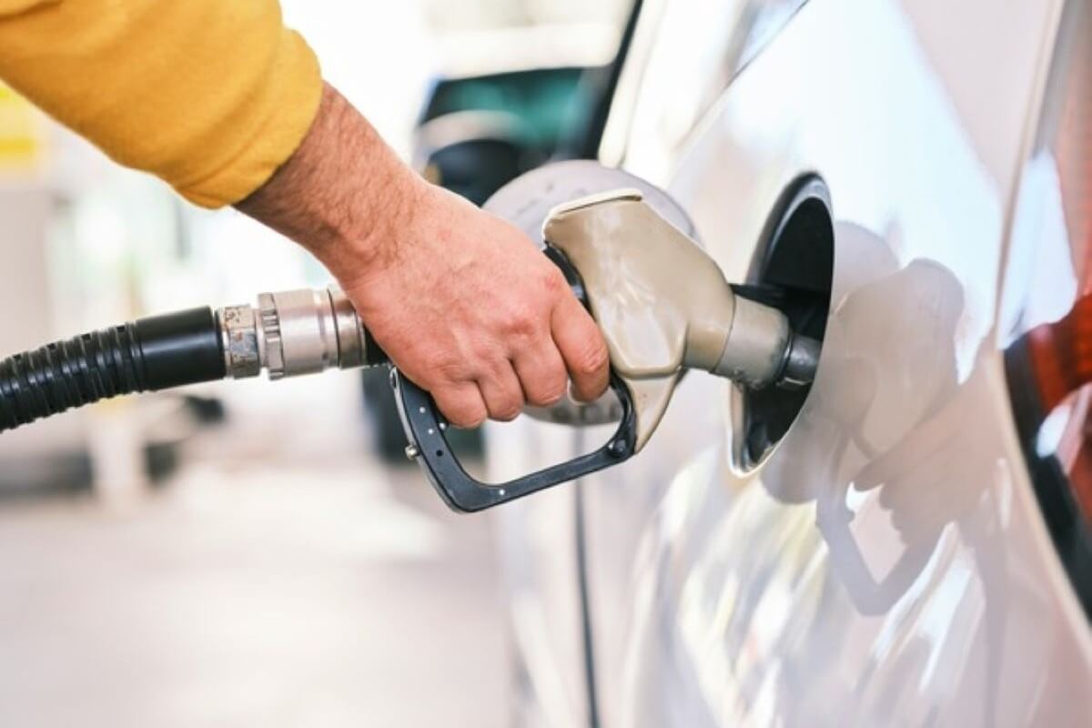 Driver refuelling a vehicle at a petrol station, comparing fuel costs with electric vehicles.