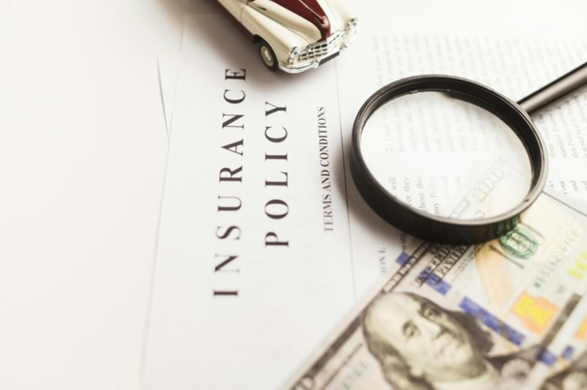 Car insurance policy with a model car and magnifying glass, highlighting insurance considerations for electric vehicles.