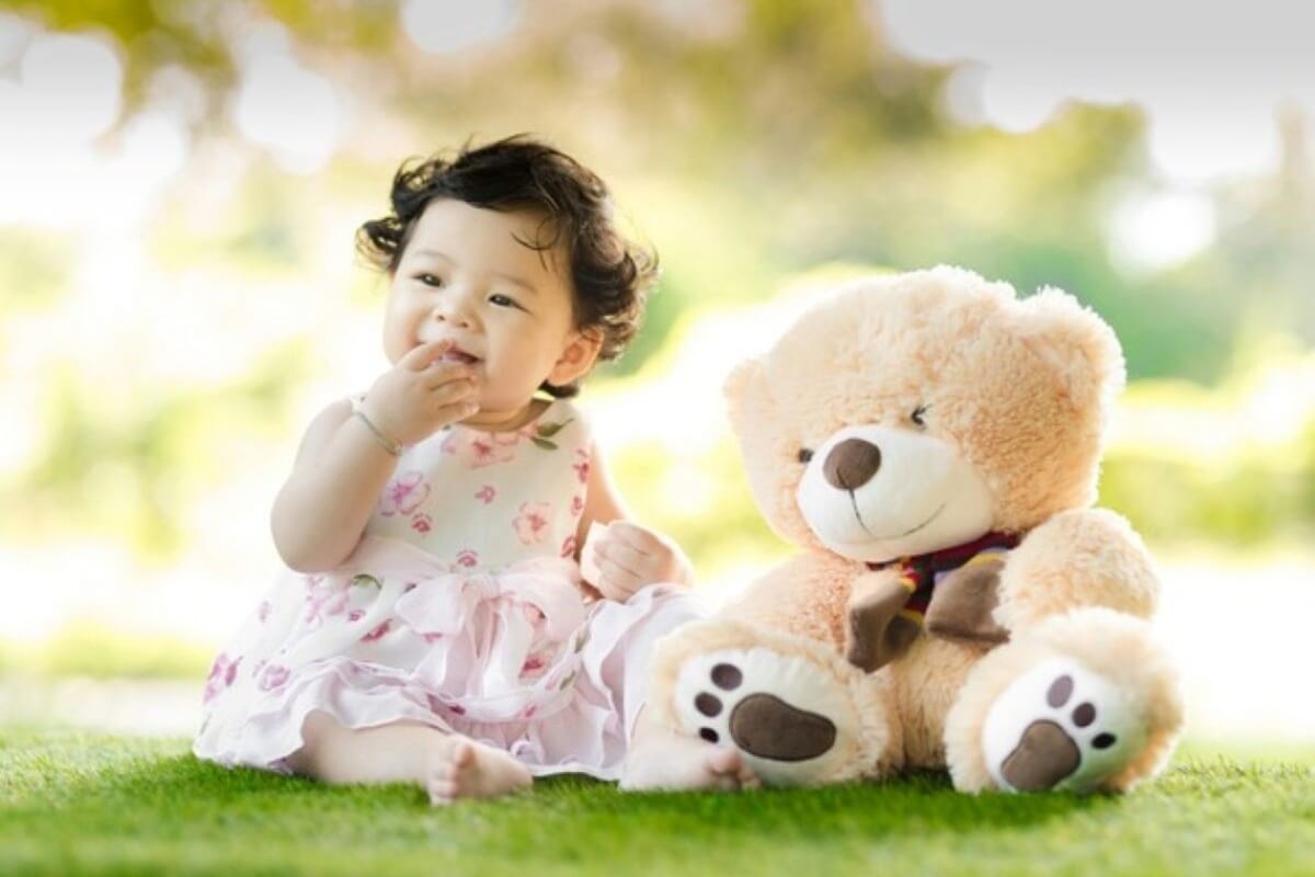 Young child sitting beside a teddy bear, highlighting the value of starting early to make your child a millionaire.