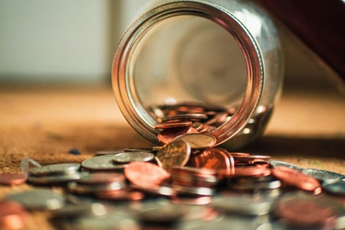 Coins spilling from a glass jar, representing consistent saving and investing to make your child a millionaire.