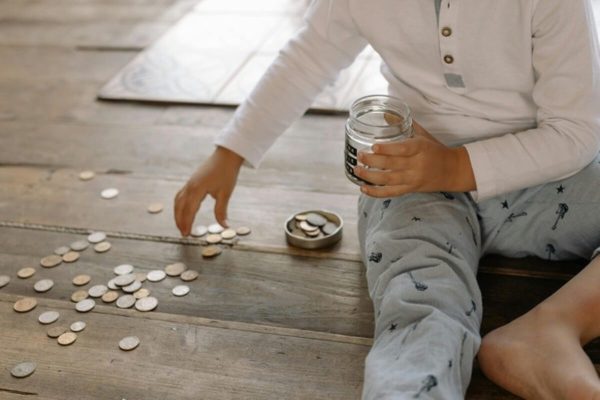 Child collecting coins in a jar, illustrating the saving habits needed to make your child a millionaire.