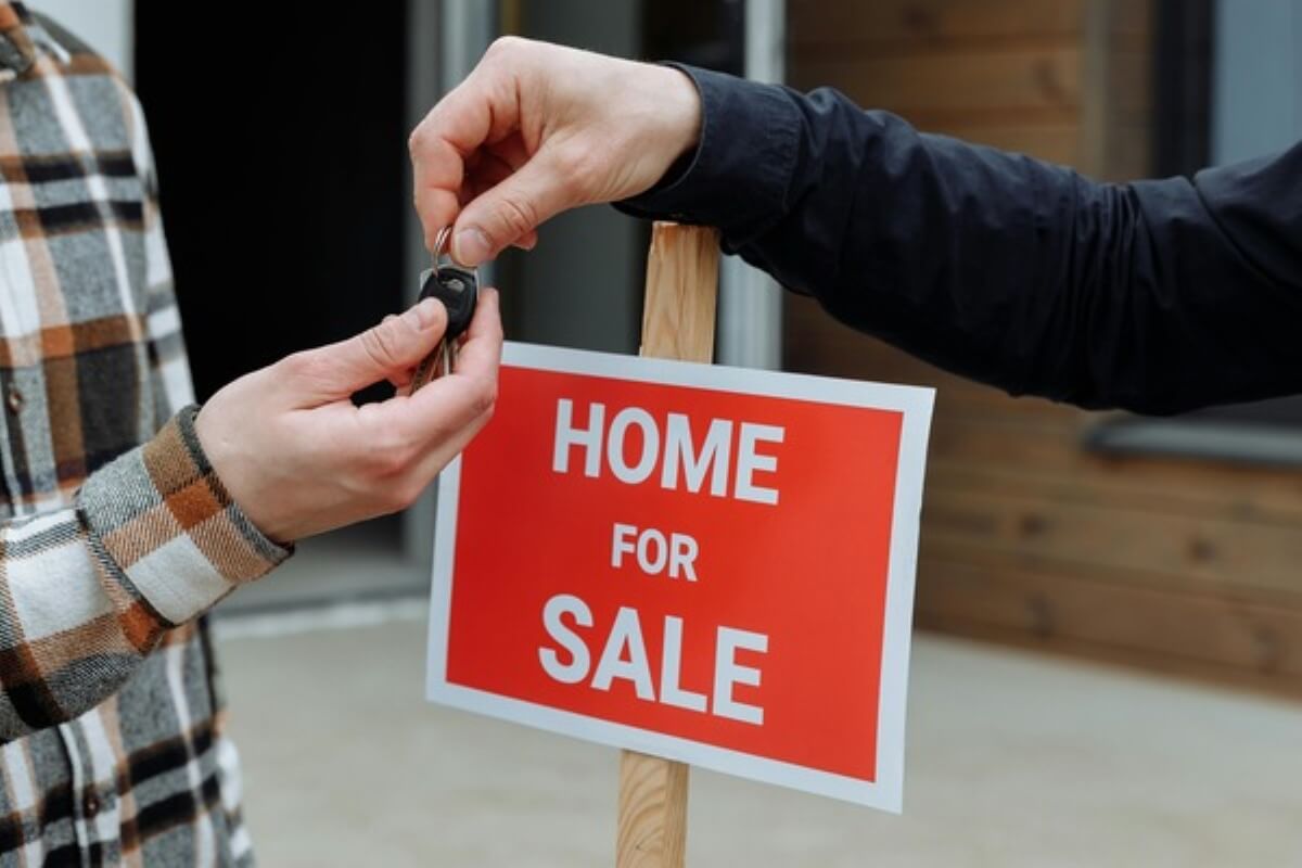 New homeowner receiving house keys beside a home for sale sign after successfully buying property under construction.