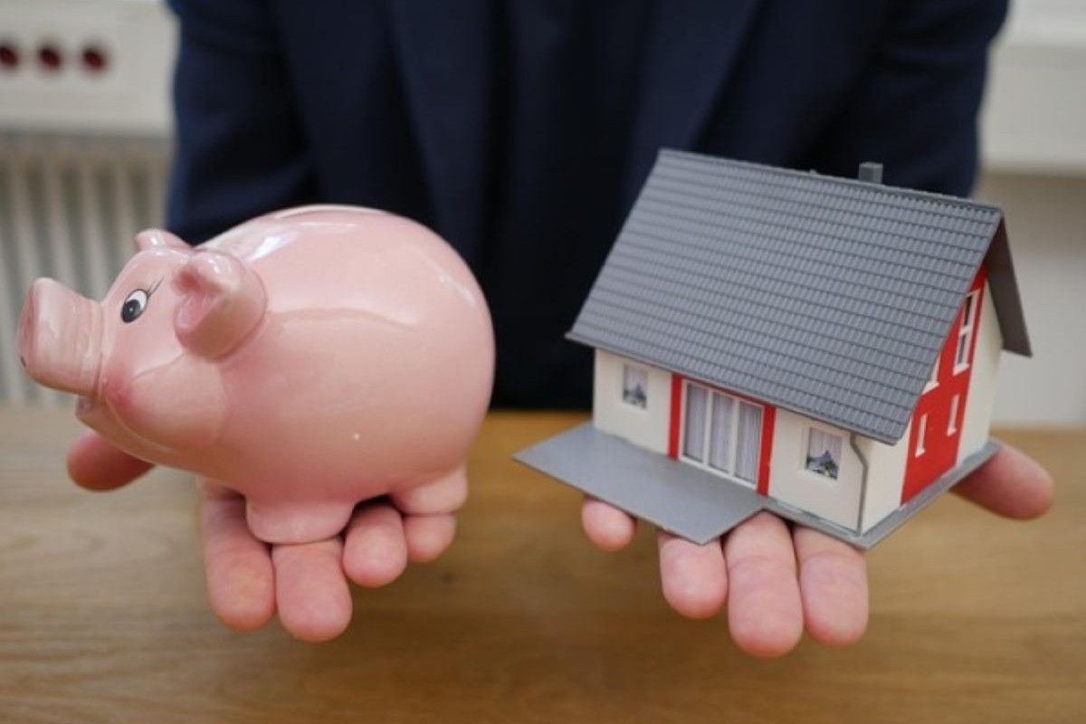 Piggy bank and model house held side by side, symbolising saving for the deposit when buying property under construction.