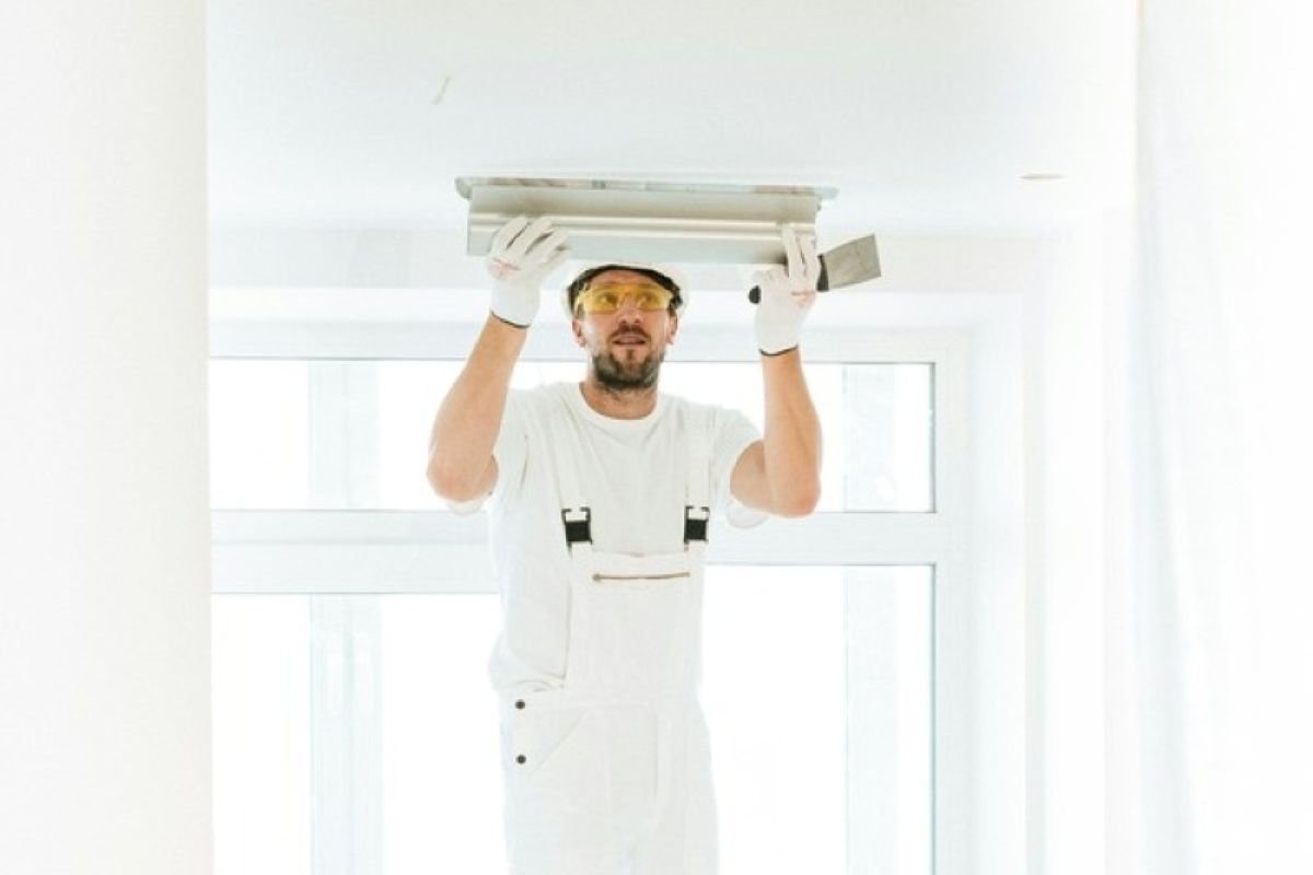 Worker installing a ceiling fixture in a newly built home, representing the final stages of buying property under construction before handover.