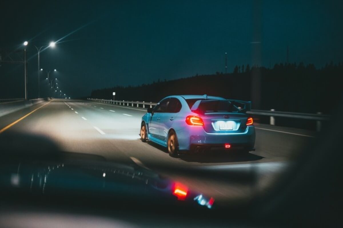 Blue car driving on a highway at night with headlights on, representing safe driving and choosing the right Singapore car insurance.