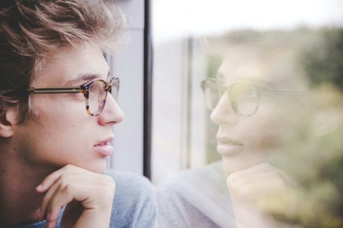 Thoughtful person looking at their reflection while experiencing imposter syndrome.