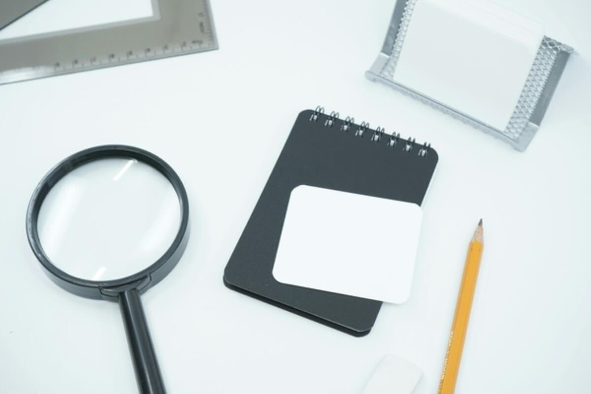 Magnifying glass and blank notebook representing self-reflection on imposter syndrome.