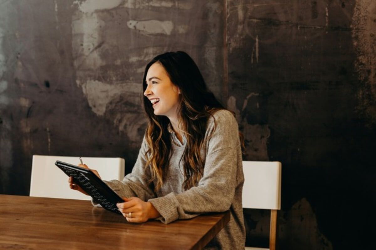 Smiling woman writing notes to build confidence and overcome imposter syndrome.