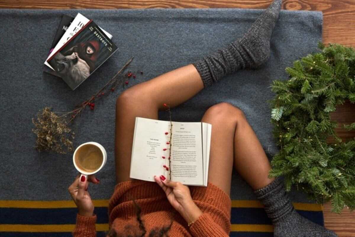 Woman relaxing with a book and coffee as a way to manage imposter syndrome.