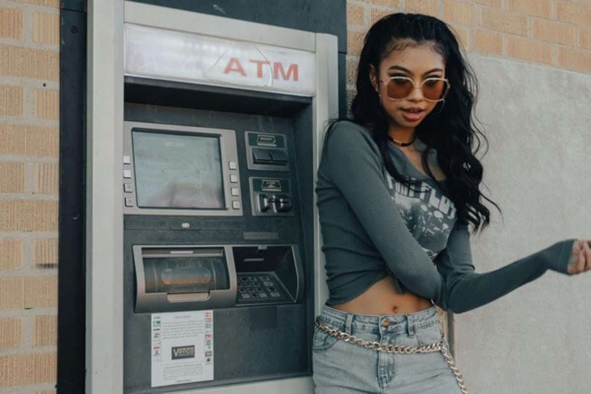 Woman beside an ATM considering withdrawals and retirement planning expenses.