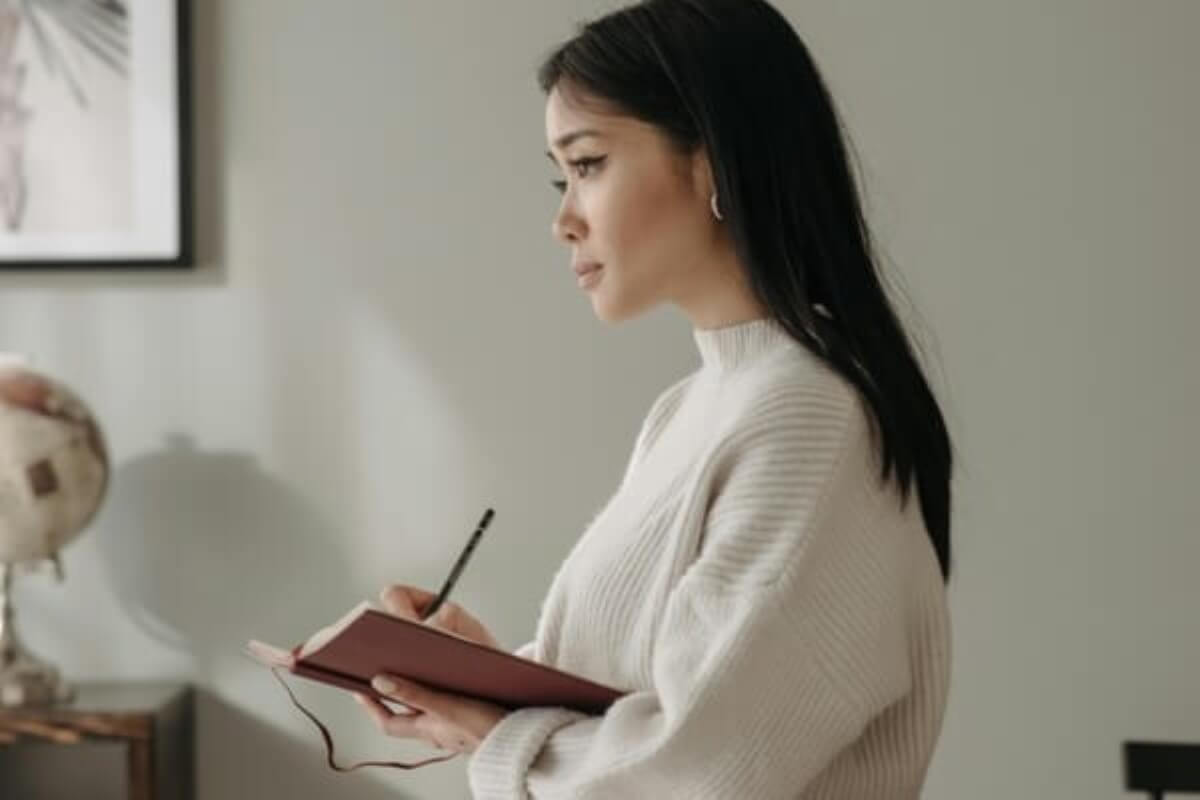 Woman writing in a notebook while considering retirement planning and future goals.
