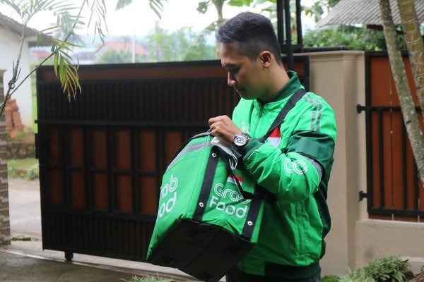 A photo of a man wearing a green long-sleeves jacket holding a green delivery bag