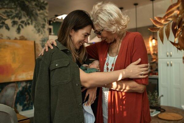 A photo of a woman and an elderly woman both hugging a newborn