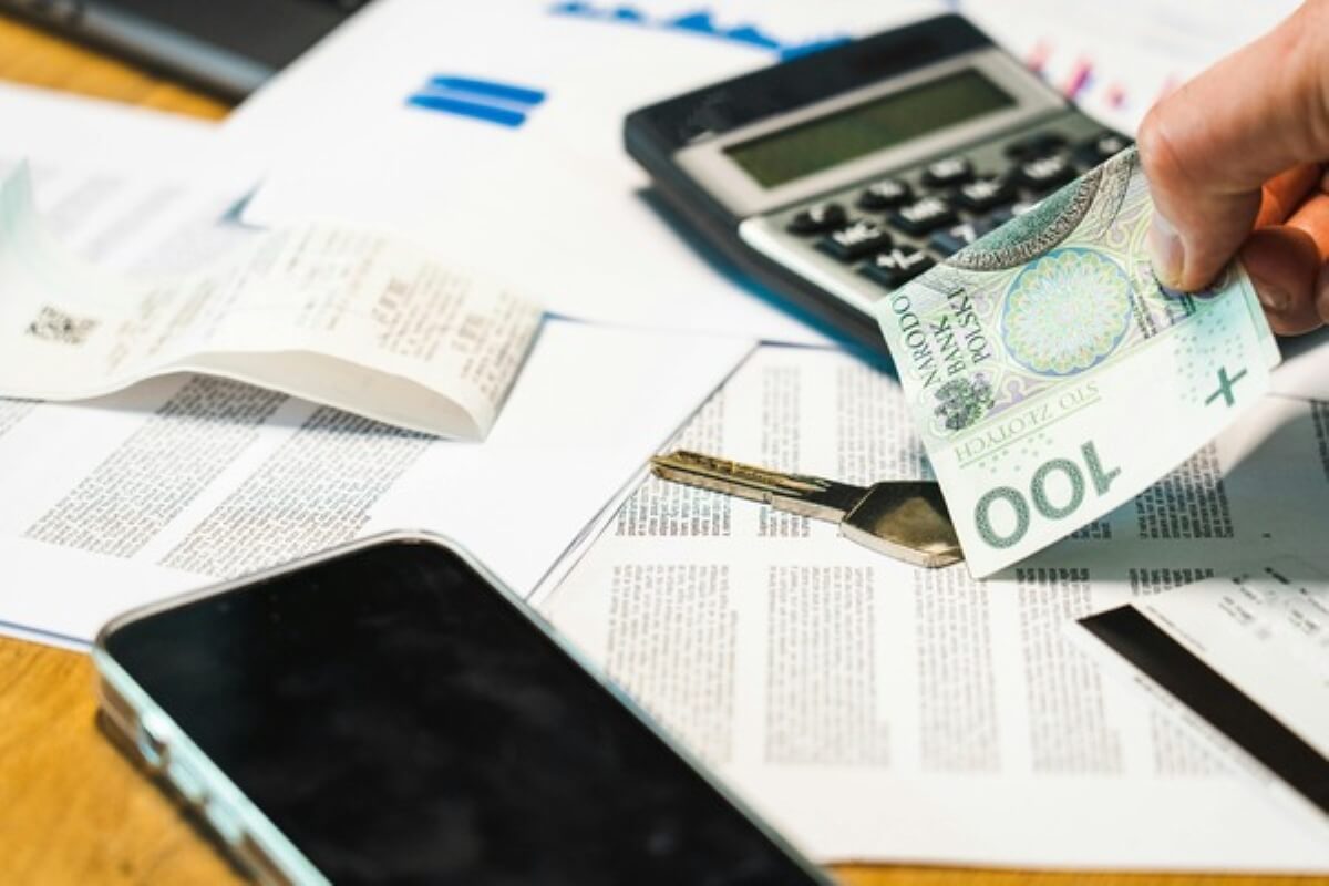 Person paying bills with cash beside financial documents and a calculator while budgeting for higher costs from trump tariff.