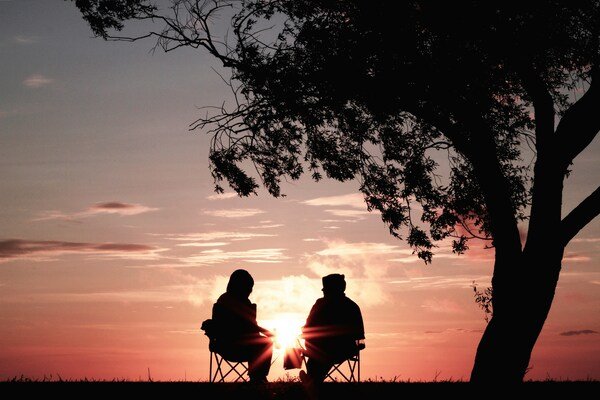 A photo of a silhouette of two person sitting on chair near tree