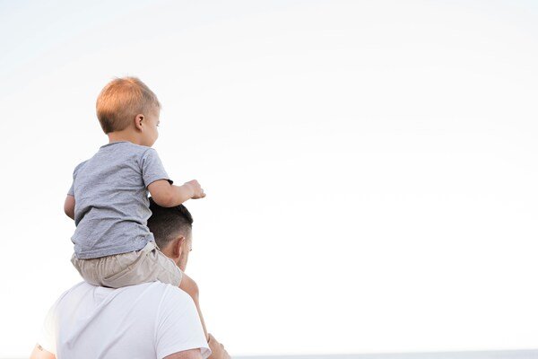 A photo of a man in white shirt carrying a child on his shoulders