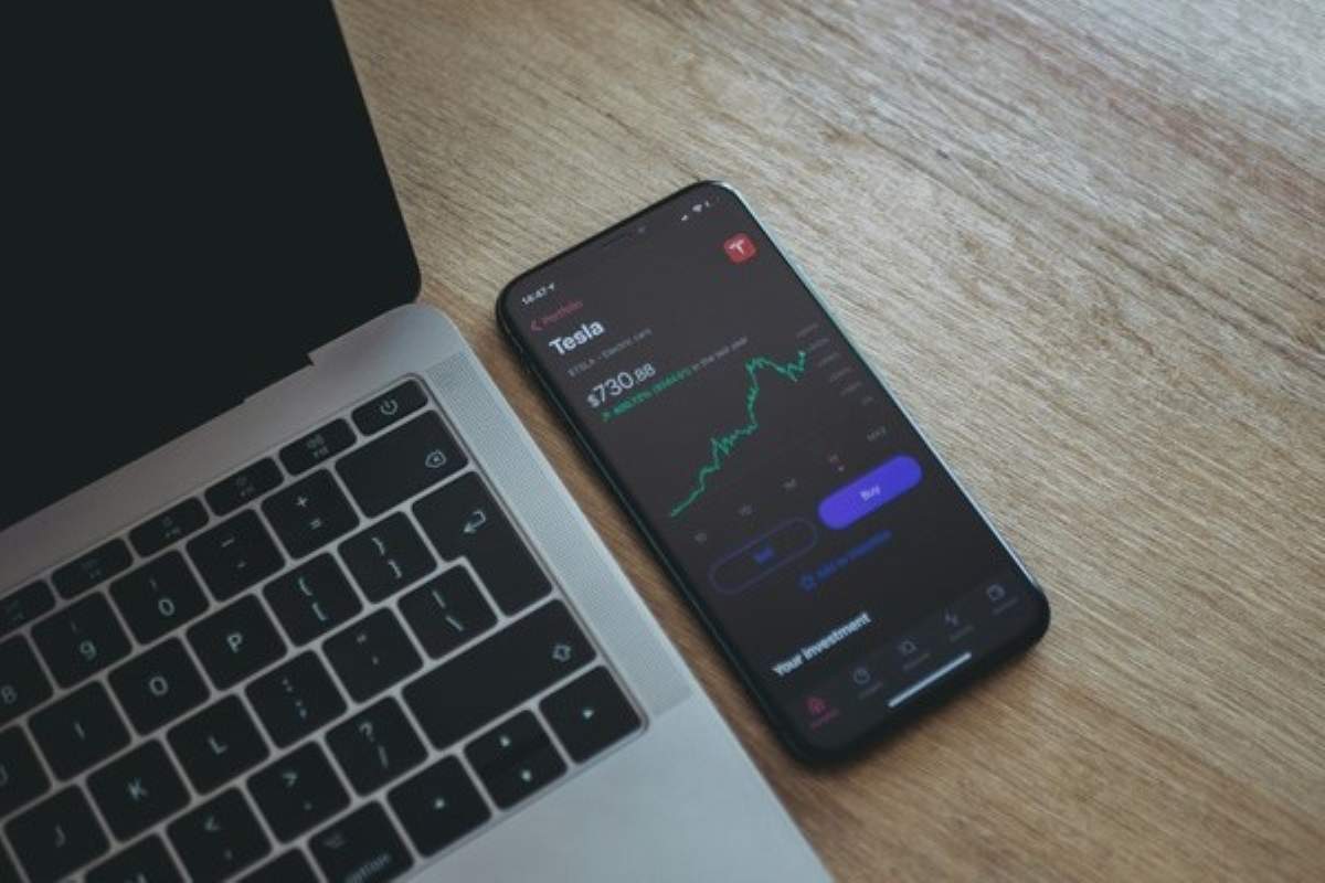 Smartphone displaying a rising stock chart beside a laptop, illustrating AI investing through a mobile investment app.