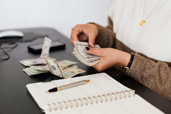 A photo of a person counting paper bills and writing on a notebook