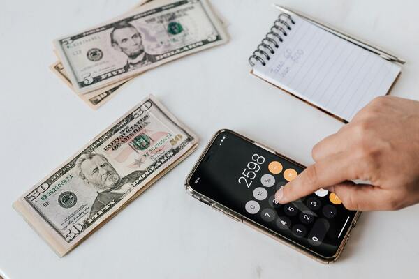 A photo of a person's hand using phone calculator while counting paper bills