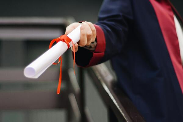 A close-up photo of a person wearing a graduation gown and holding a white scroll