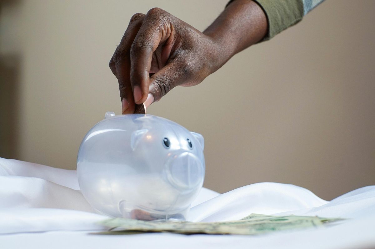 Hand placing coins into a piggy bank as part of a money market funds savings strategy.