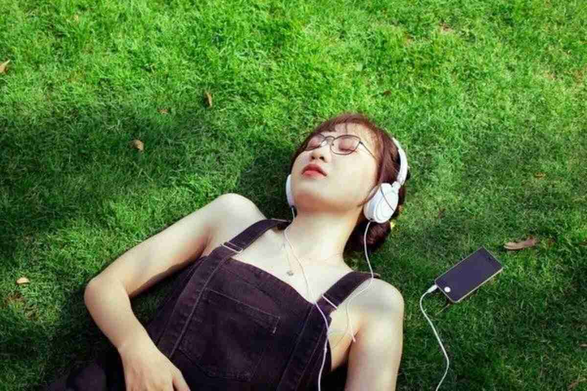 Woman relaxing on the grass with headphones, showing healthy habits for how to improve sleep quality.