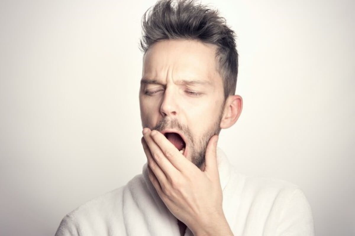 Sleepy man yawning from fatigue, emphasising the importance of how to improve sleep quality.