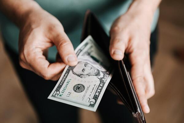 A close-up photo of a person's hand getting money from a black wallet