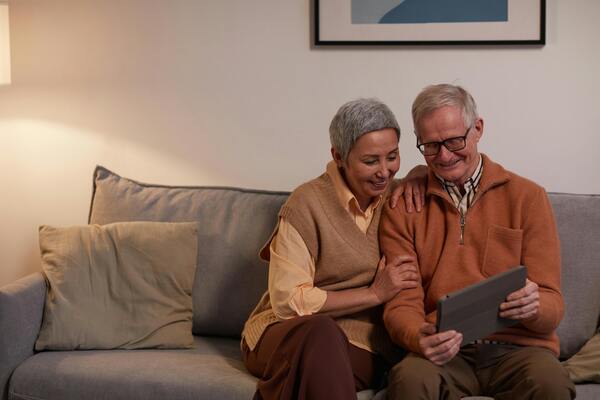 A photo of a senior couple sitting on a sofa while both looking at a gadget