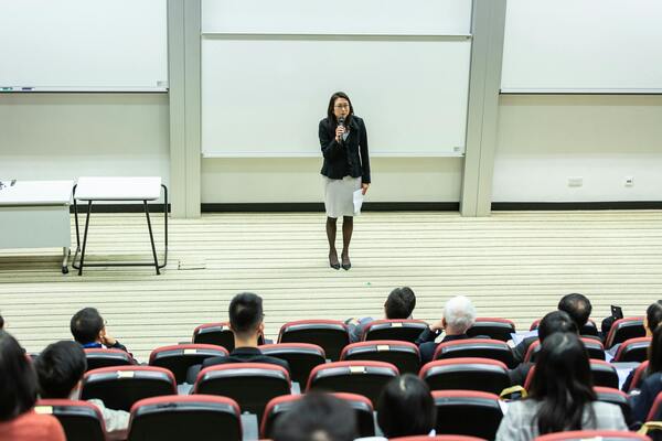 A photo of a woman speaking in front of the people in a private room