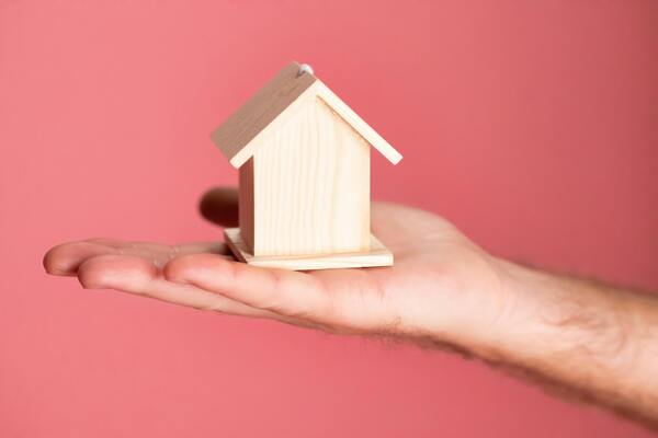 A photo of a person's hand holding out a miniature wooden house