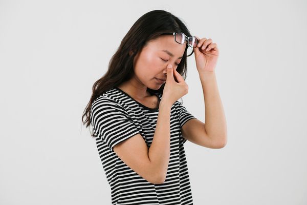Woman rubbing her eyes after removing her glasses, illustrating common vision problems before LASIK in Singapore.