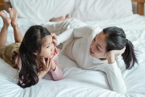 A photo of a woman talking to a young girl child on a bed