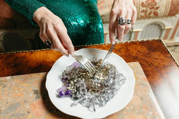 A photo of a woman's hands holding a fork and knife, mimicking the act of cutting jewelry on a plate as if it were food