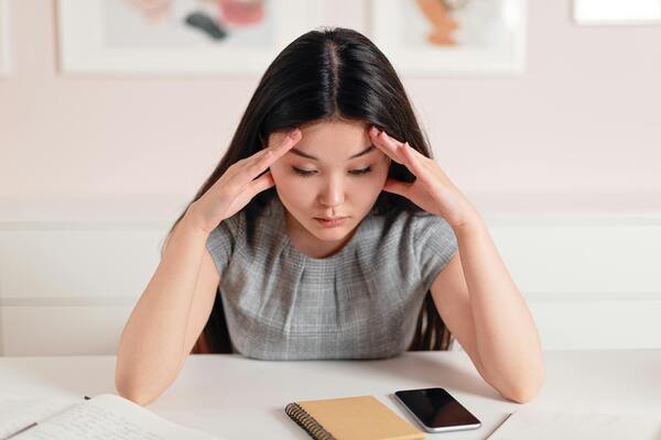 A photo of a woman staring at her phone on the table with her hands on her hand as a sign of thinking