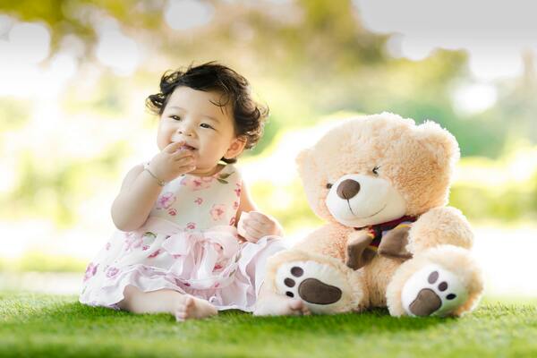 A photo of a baby girl in pink dress sitting beside a teddy bear stuffed toy