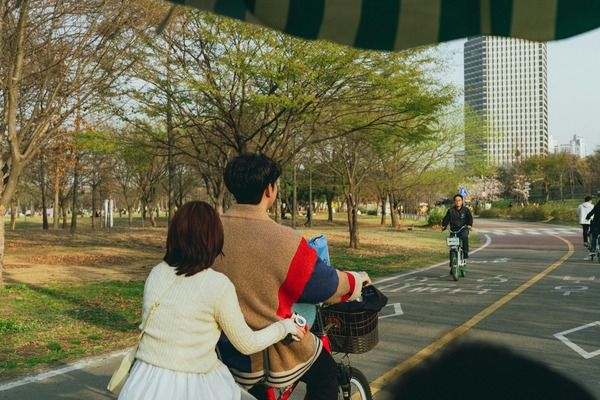 Young couple cycling through a park together, reflecting on the lifestyle and financial considerations when deciding should you have kids.