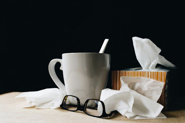 A photo of a white ceramic mug on the table beside a black eyeglass and a bunch of tissue papers