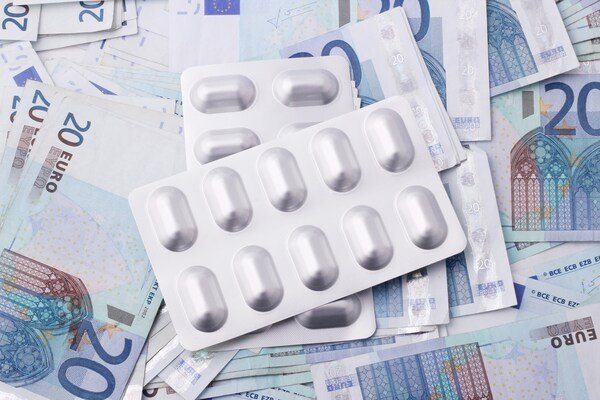 A flat lay photo of medicine tablets placed on scattered paper bills