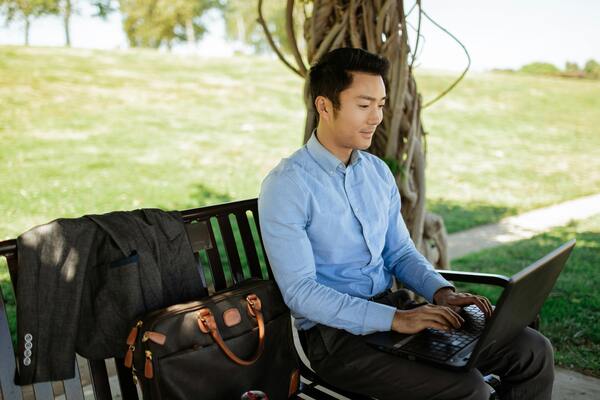 A photo of a man sitting on a bench using a laptop