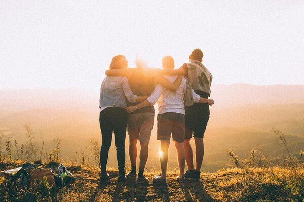 Four people with arms around each other’s shoulders watching the sunset