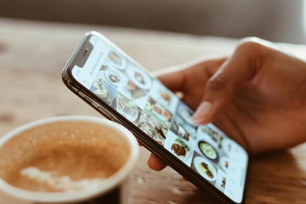 Close-up of a person’s hand holding an iPhone, with the home screen apps in sharp focus while the background fades out.
